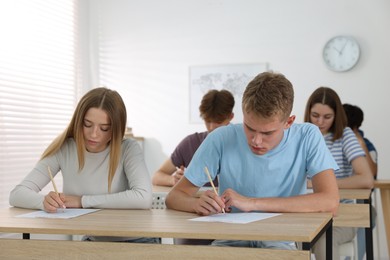 Photo of Students taking exam at wooden table indoors