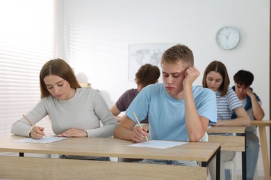 Photo of Students taking exam at wooden table indoors