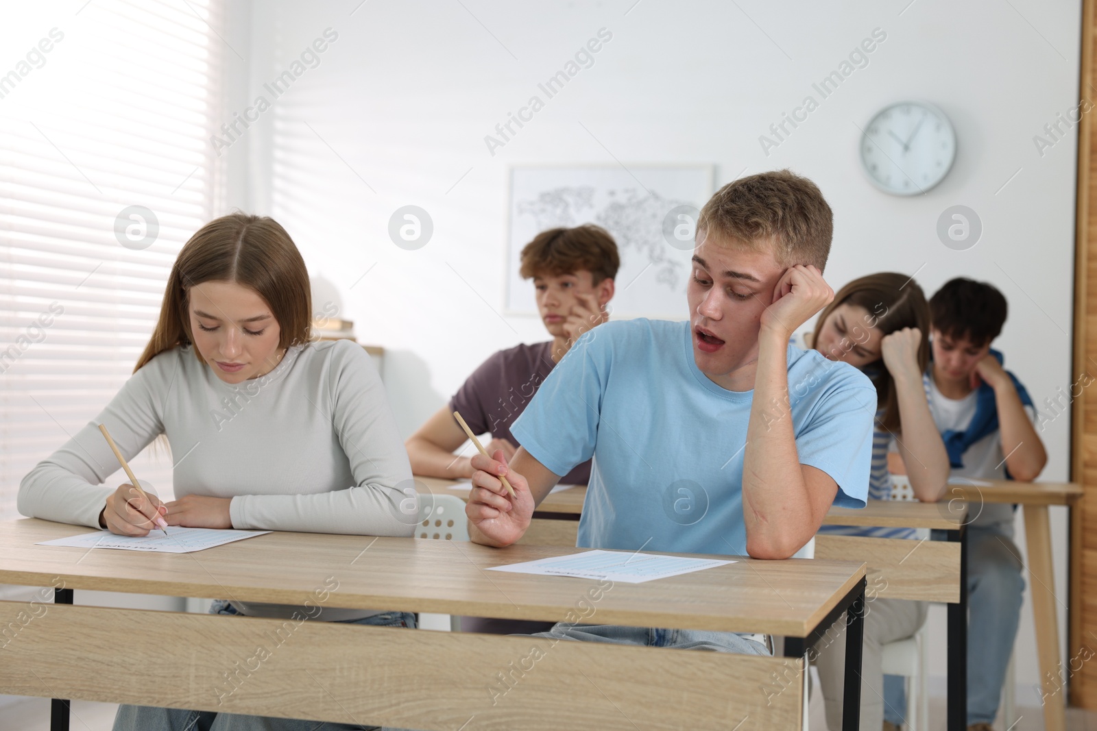 Photo of Students taking exam at wooden table indoors
