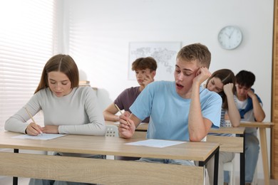 Photo of Students taking exam at wooden table indoors