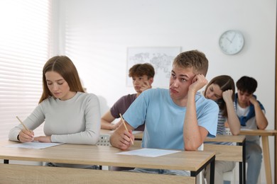 Photo of Students taking exam at wooden table indoors