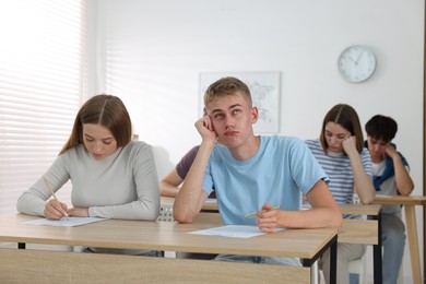 Photo of Students taking exam at wooden table indoors
