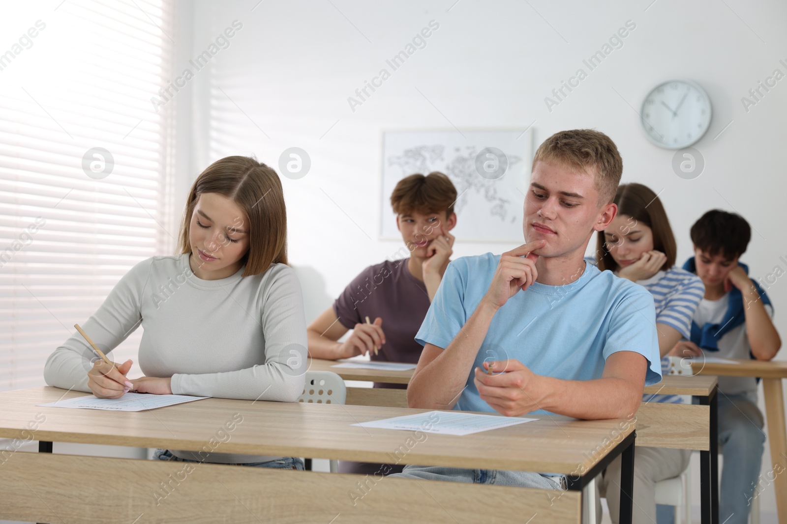 Photo of Students taking exam at wooden table indoors