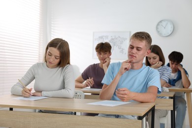 Photo of Students taking exam at wooden table indoors