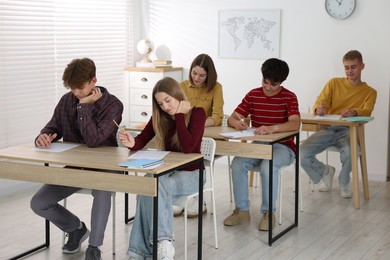 Photo of Students taking exam at wooden table indoors