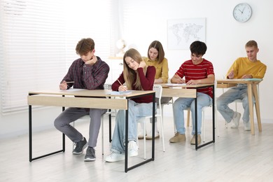 Photo of Students taking exam at wooden table indoors