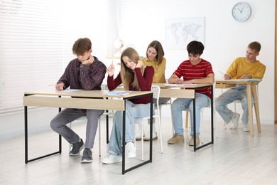 Photo of Students taking exam at wooden table indoors
