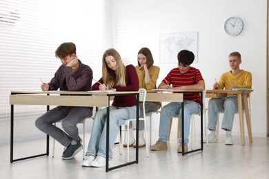 Photo of Students taking exam at wooden table indoors