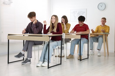 Photo of Students taking exam at wooden table indoors