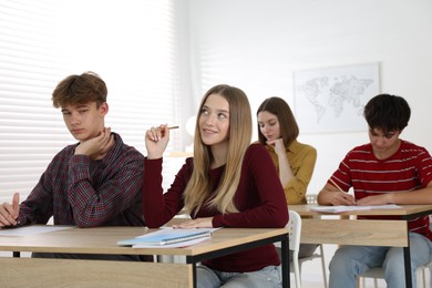 Photo of Students taking exam at wooden table indoors