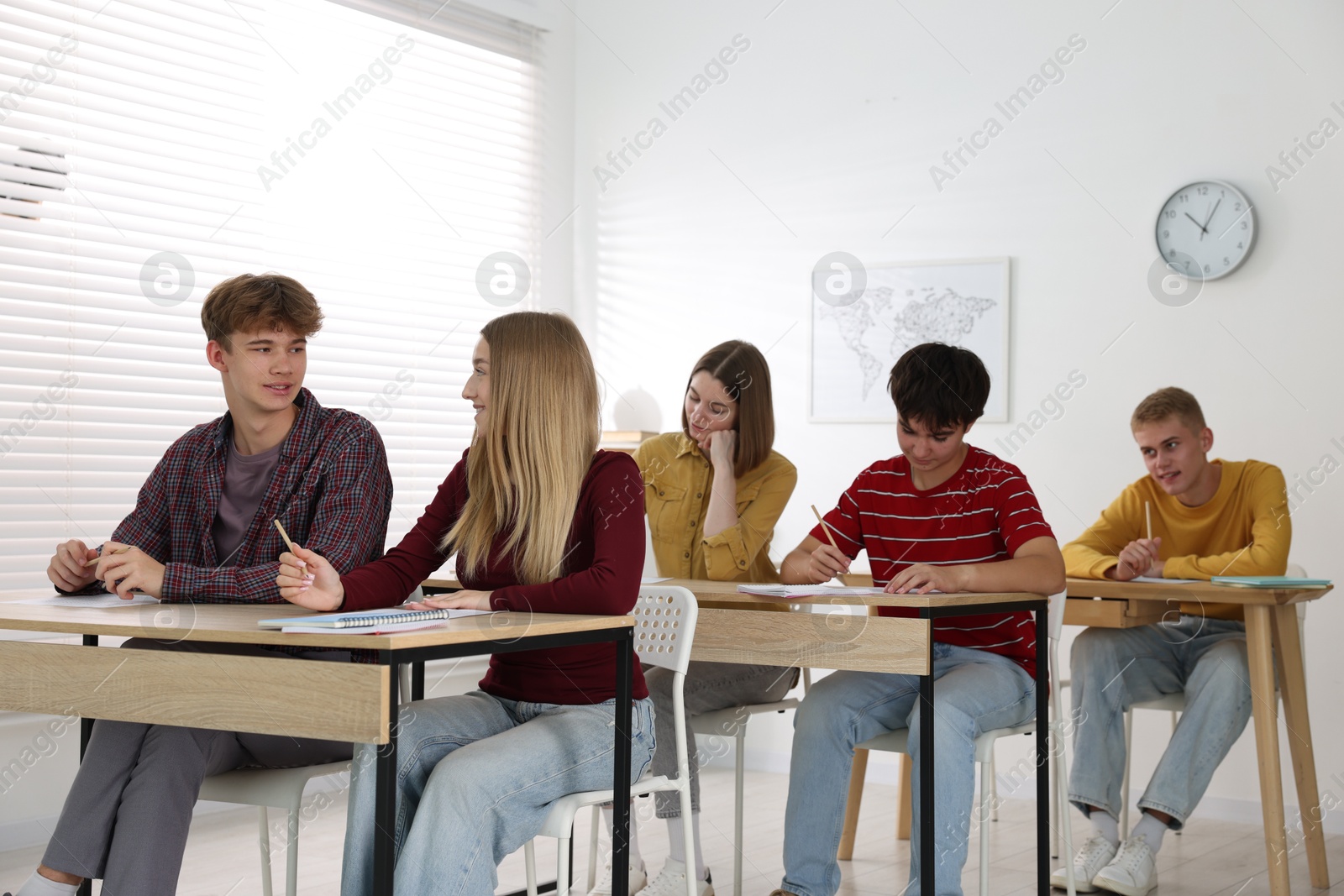 Photo of Students taking exam at wooden table indoors