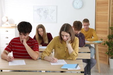Photo of Students taking exam at wooden table indoors