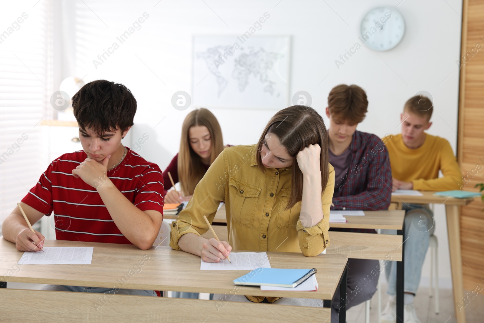 Photo of Students taking exam at wooden table indoors