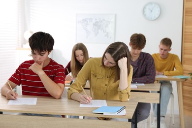 Photo of Students taking exam at wooden table indoors