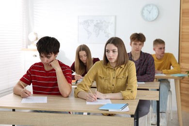 Photo of Students taking exam at wooden table indoors