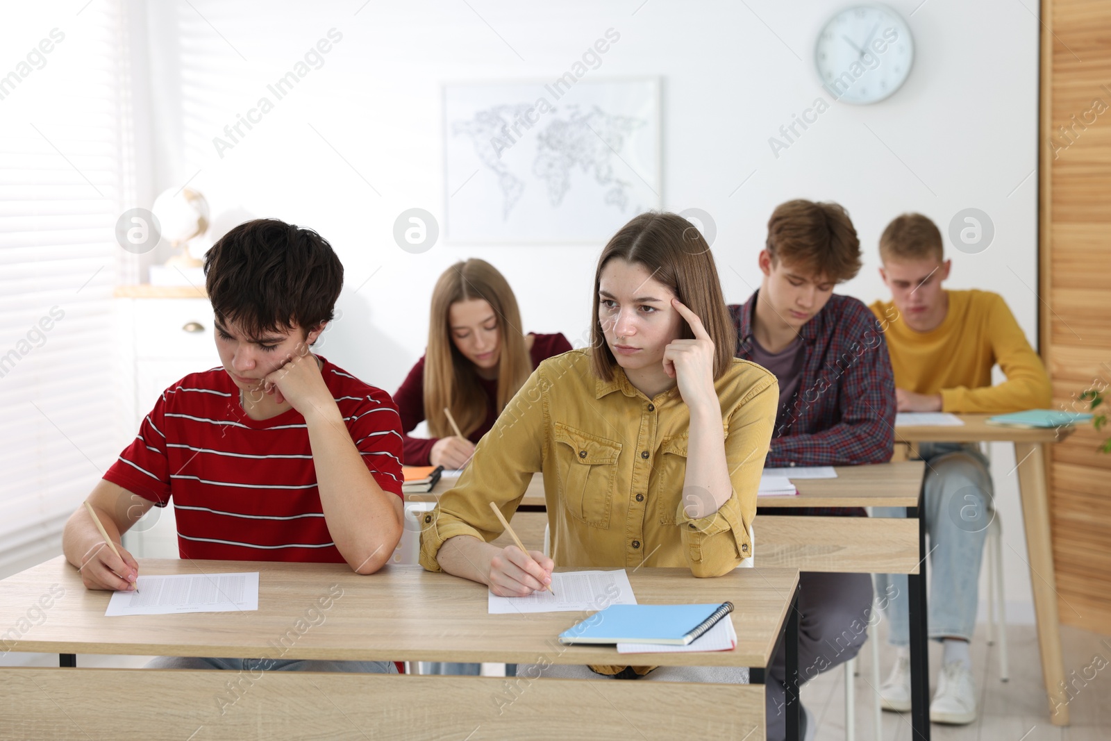 Photo of Students taking exam at wooden table indoors