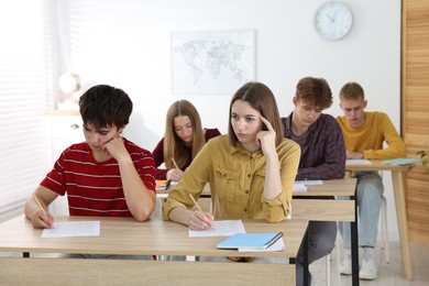 Photo of Students taking exam at wooden table indoors