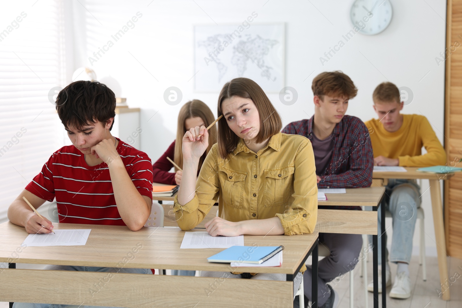 Photo of Students taking exam at wooden table indoors