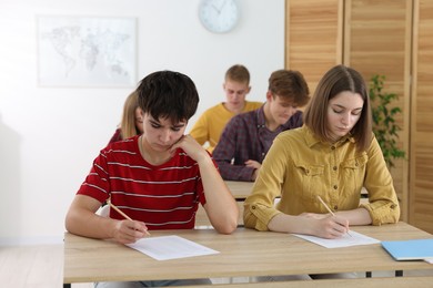 Photo of Students taking exam at wooden table indoors