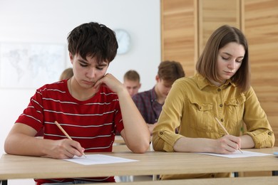 Photo of Students taking exam at wooden table indoors