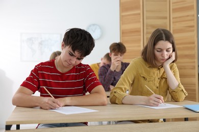 Photo of Students taking exam at wooden table indoors