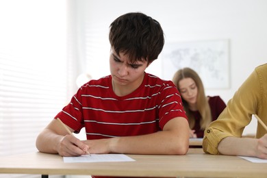 Photo of Students taking exam at wooden table indoors, selective focus