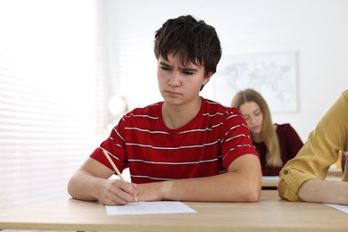 Photo of Students taking exam at wooden table indoors, selective focus