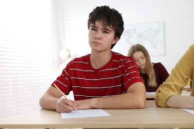 Photo of Students taking exam at wooden table indoors, selective focus