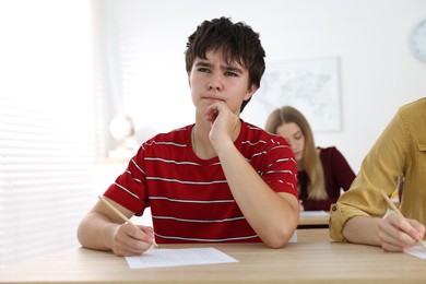Photo of Students taking exam at wooden table indoors, selective focus