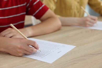 Photo of Students filling out answer sheet at wooden table indoors, closeup. Taking exam