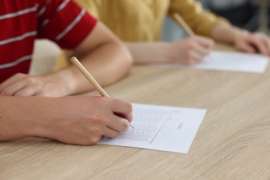 Photo of Students filling out answer sheet at wooden table indoors, closeup. Taking exam
