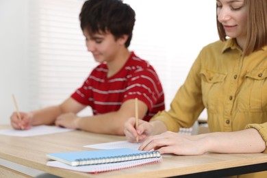 Photo of Students taking exam at wooden table indoors, selective focus
