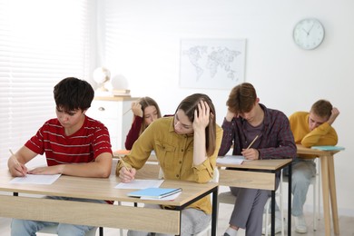 Photo of Students taking exam at wooden table indoors