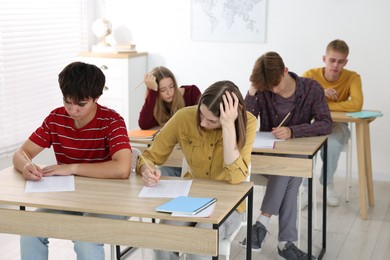 Photo of Students taking exam at wooden table indoors