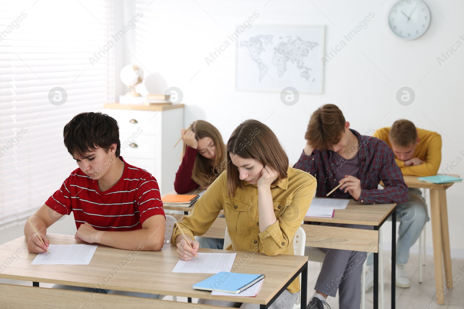 Photo of Students taking exam at wooden table indoors