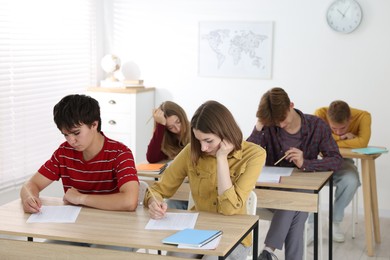Photo of Students taking exam at wooden table indoors