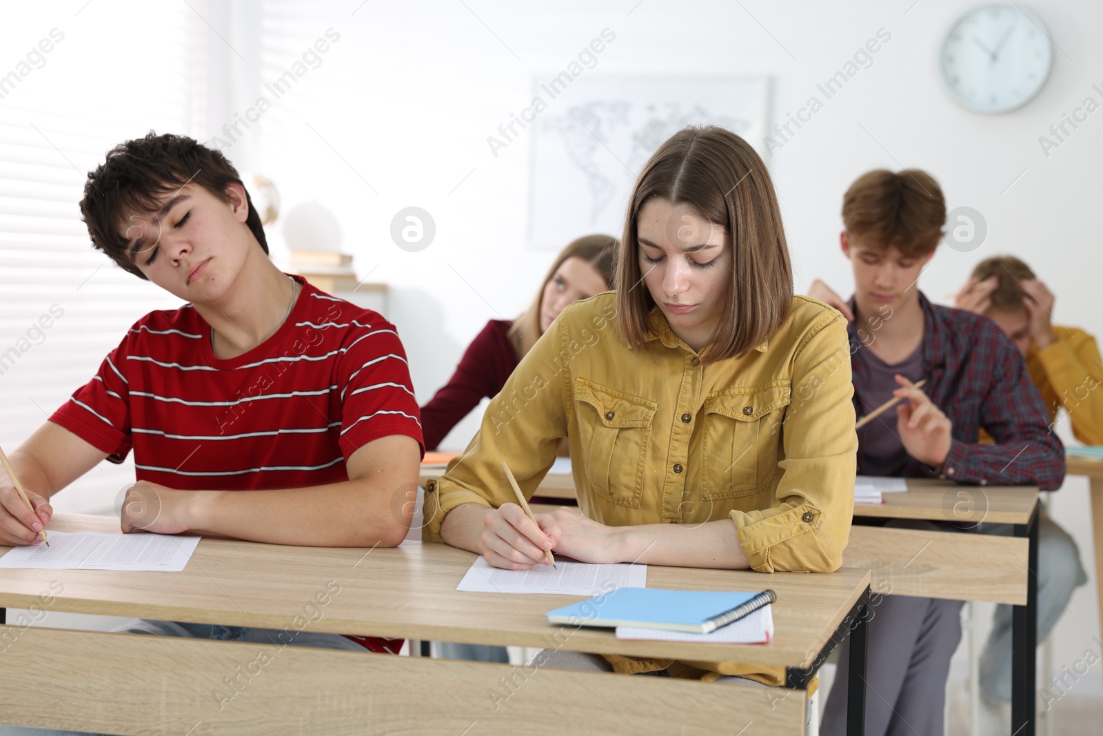 Photo of Students taking exam at wooden table indoors