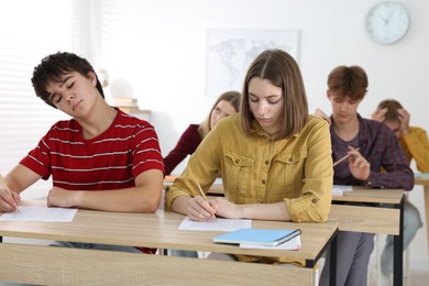 Photo of Students taking exam at wooden table indoors