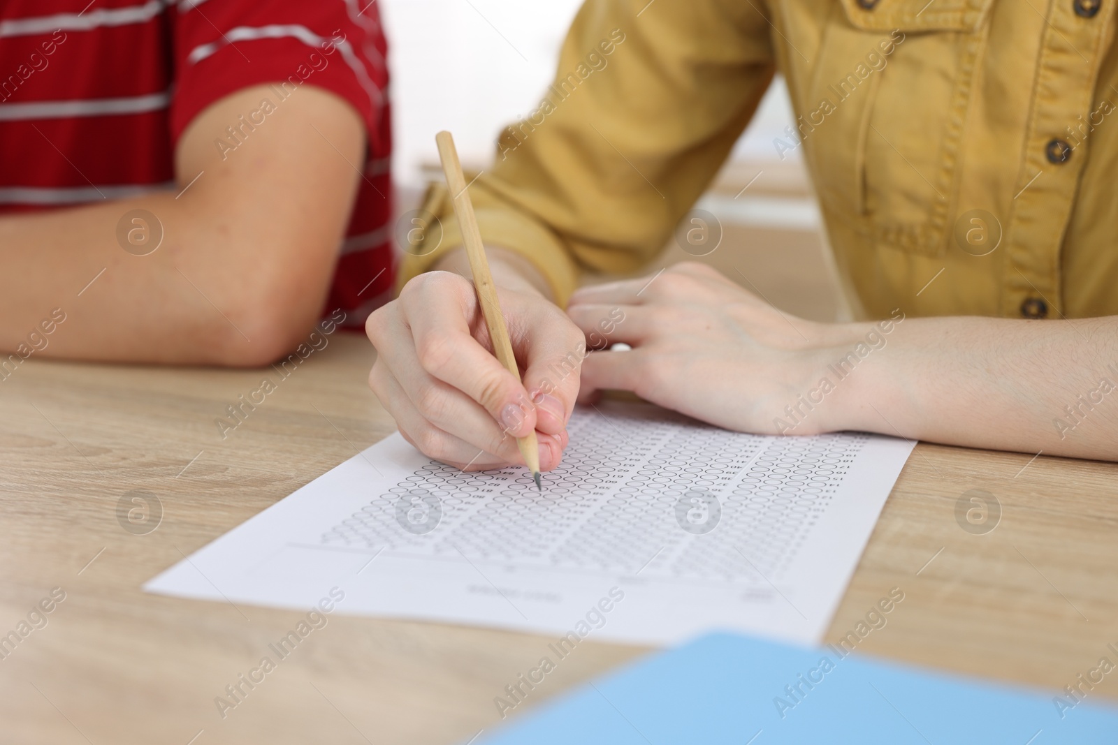 Photo of Students taking exam at wooden table indoors, closeup