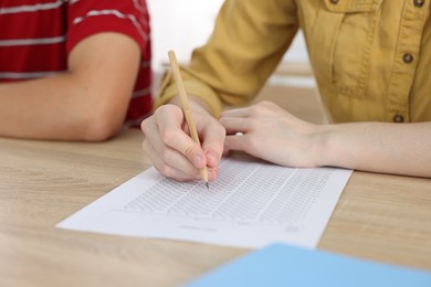 Photo of Students taking exam at wooden table indoors, closeup