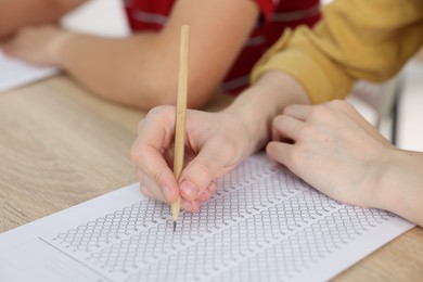Photo of Students taking exam at wooden table indoors, closeup