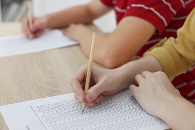 Photo of Students taking exam at wooden table indoors, closeup