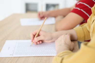 Photo of Students taking exam at wooden table indoors, closeup