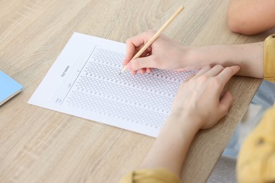 Photo of Student taking exam at wooden table indoors, closeup
