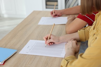 Photo of Students taking exam at wooden table indoors, closeup