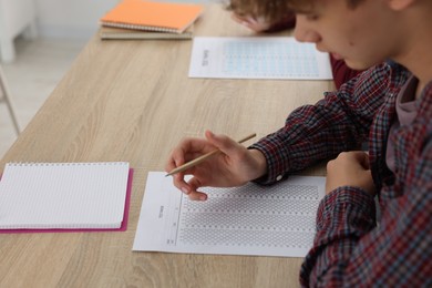 Photo of Student taking exam at wooden table indoors, selective focus