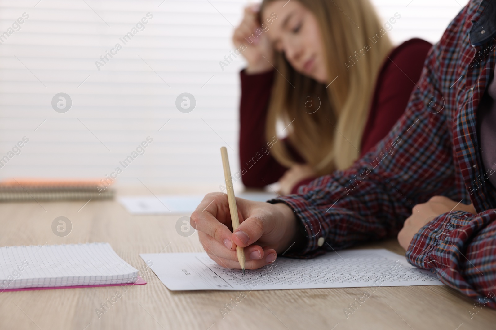 Photo of Students taking exam at wooden table indoors, selective focus