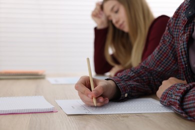 Photo of Students taking exam at wooden table indoors, selective focus