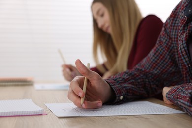 Photo of Students taking exam at wooden table indoors, selective focus