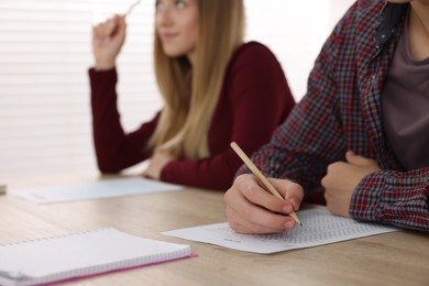 Photo of Students taking exam at wooden table indoors, selective focus